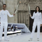 SAINT-DENIS, FRANCE - JULY 26: France Televisions' TV host and journalist Mohamed Bouhafsi (L) and French actress Laetitia Casta hold the Olympic Torch as part of the 2024 Paris Olympic Games Torch Relay, on the day of the opening ceremony, on July 26, 2024 in Saint-Denis, outside Paris. (Photo by Stephane De Sakutin - Pool/Getty Images)