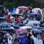 PARIS, FRANCE - JULY 26: Spectators hold umbrellas as they watch the floating parade from the banks of the River Seine during the Opening Ceremony of the Olympic Games Paris 2024 on July 26, 2024, in Paris, France. (Photo by Clodagh Kilcoyne - Pool/Getty Images)