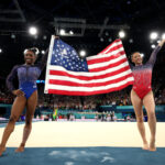 PARIS, FRANCE - AUGUST 01: Gold medalist Simone Biles (L) and Bronze medalist Sunisa Lee of Team United States celebrate with the American flag after competing in the Artistic Gymnastics Women's All-Around Final on day six of the Olympic Games Paris 2024 at Bercy Arena on August 01, 2024 in Paris, France. (Photo by Jamie Squire/Getty Images)